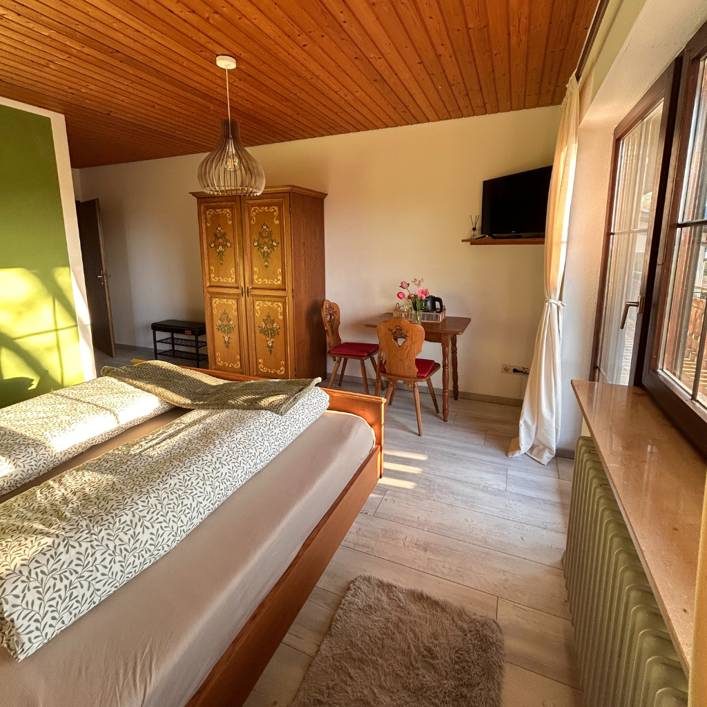Gemütliches Gästezimmer im Lindenhof mit traditionellem Holzschrank, Sitzgelegenheit und großem Fenster