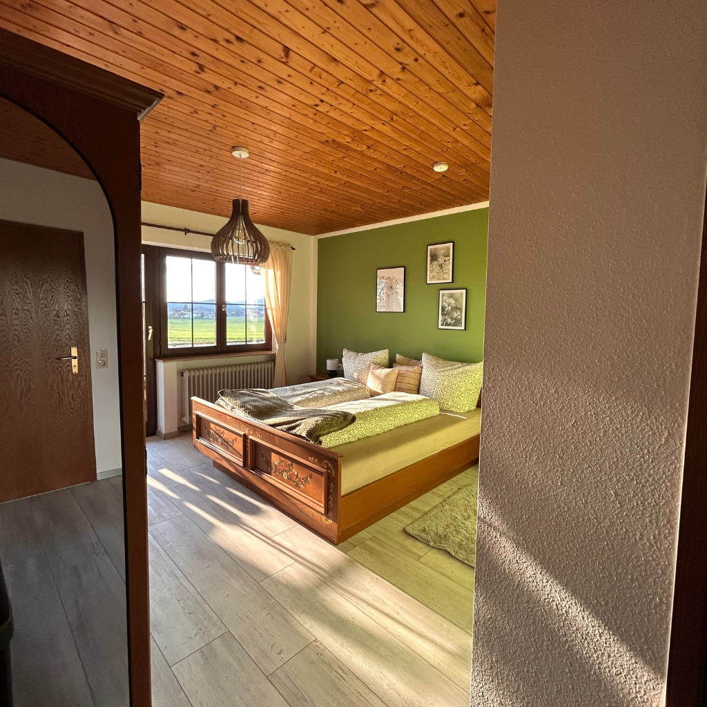 Schlafzimmer im Lindenhof Worblingen mit Doppelbett, grüner Wand, Holzmöbeln und Blick ins Grüne