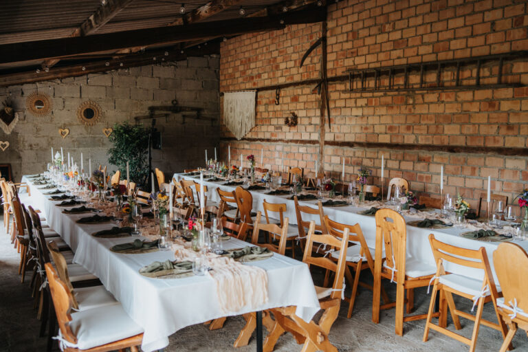 Festlich gedeckte Tische in der Scheune des Lindenhofs, rustikale Stühle, Kerzen und Blumendeko für Hochzeit oder Event.