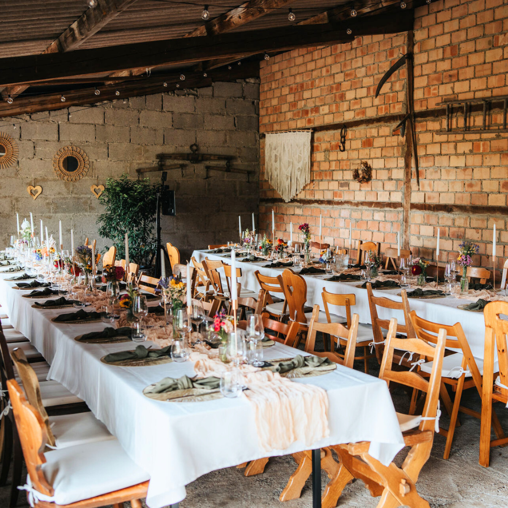 Festlich gedeckte Tische in der Scheune des Lindenhofs, rustikale Stühle, Kerzen und Blumendeko für Hochzeit oder Event.